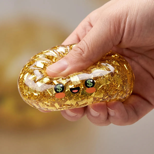 Hand squeezing the Gold Dumpling Squishy flat as a stress relief fidget toy