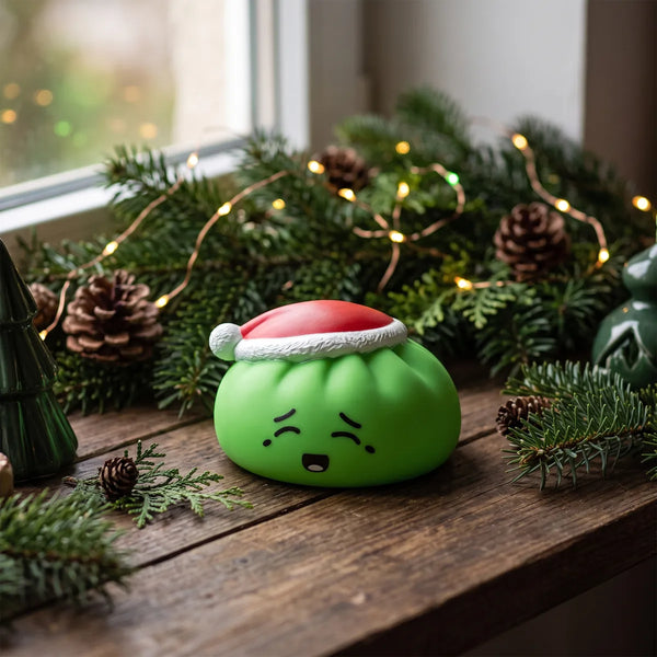 Elf Green Christmas Hat Dumpling Squishy displayed on a wooden table with pine cones and fairy lights