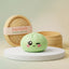 Pistachio Green Wink Dumpling Squishy on a white studio podium beside a steamer basket