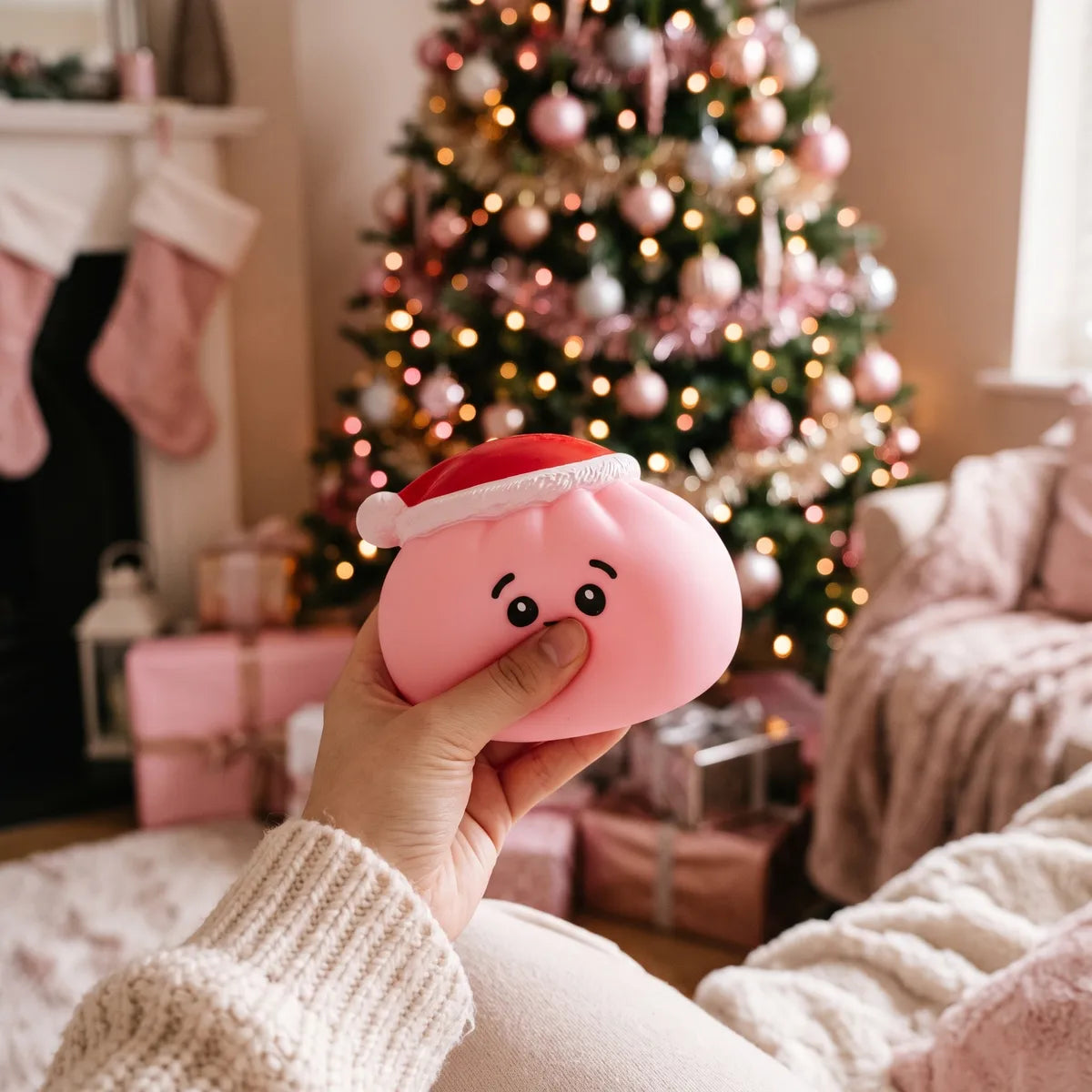 Person squeezing the Sugar Pink Christmas Hat Dumpling Squishy as a fidget toy by a pink Christmas tree