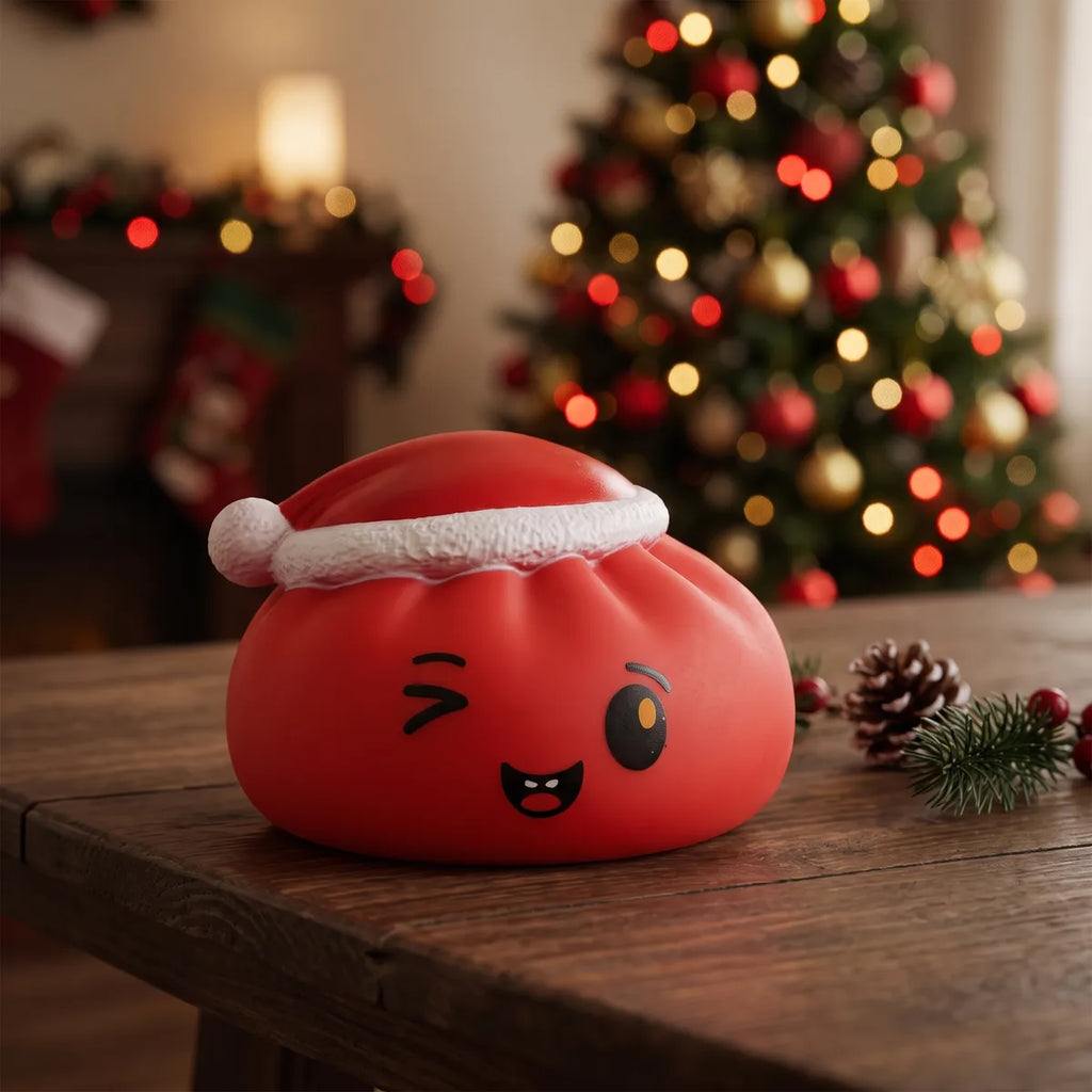 Cheeky Red Christmas Hat Dumpling Squishy displayed on a wooden table by the Christmas tree