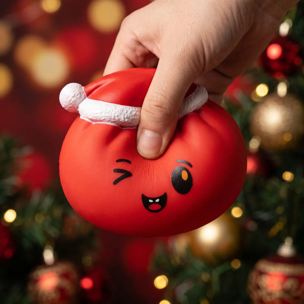 Cheeky Red Christmas Hat Dumpling Squishy pressed flat under a hand before it slowly rises back